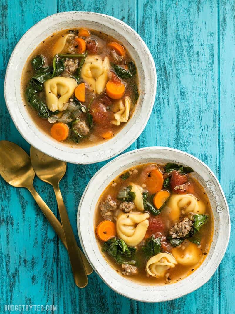 This light but filling vegetable packed Sausage and Tortelloni soup is the perfect lunch for fall. Pair with crusty bread for dipping! BudgetBytes.com Two bowls of Sausage and Tortelloni Soup on a blue background with gold spoons
