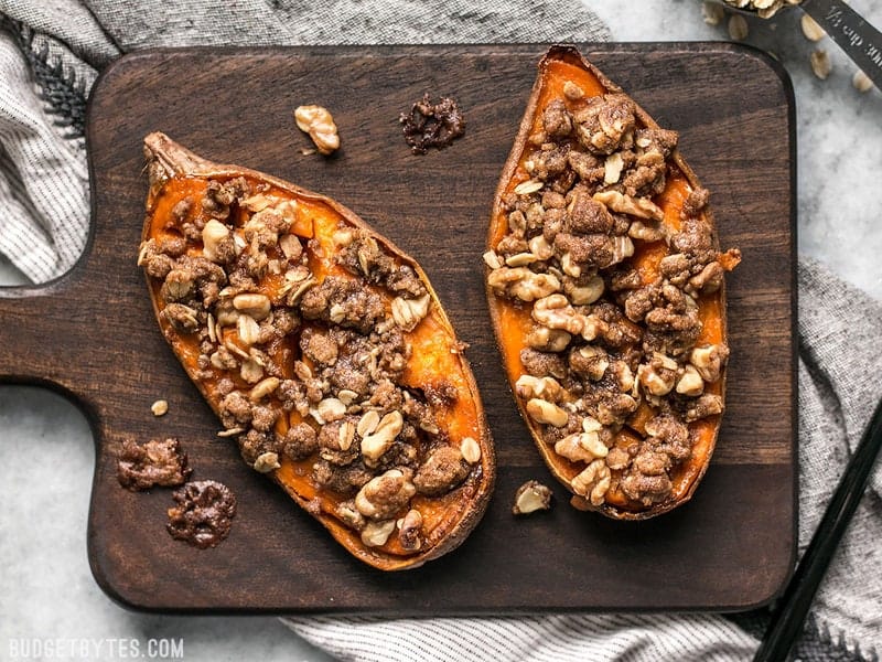 Streuseled Sweet Potatoes are an easy, deconstructed version of the classic sweet potato casserole that is manageable enough for weeknight dessert. BudgetBytes.com Overhead shot of two Streuseled Sweet Potatoes on a wooden cutting board