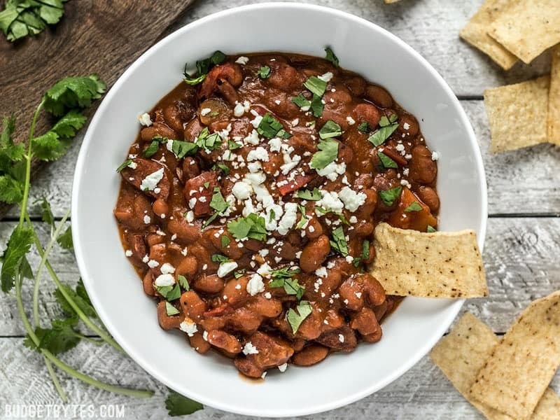 A little bit of Spanish chorizo is all it takes to turn a simple pot of pinto beans into a rich and flavorful meal! BudgetBytes.com Overhead view of Instant Pot Pinto Beans with Chorizo, topped with cheese and cilantro