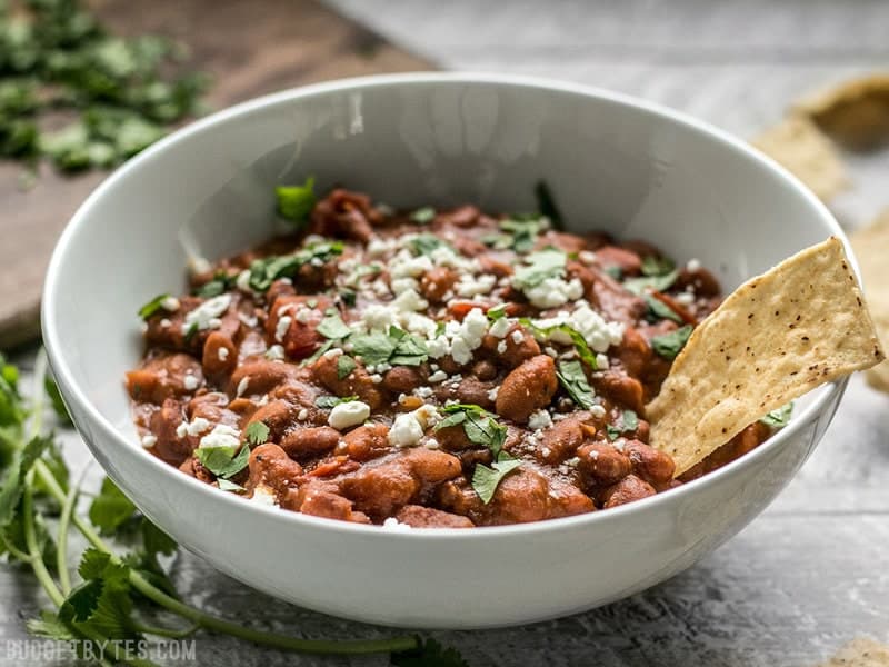 A little bit of Spanish chorizo is all it takes to turn a simple pot of pinto beans into a rich and flavorful meal! BudgetBytes.com Side view of a bowl of Instant Pot Pinto Beans with chorizo. Topped with cheese and cilantro.