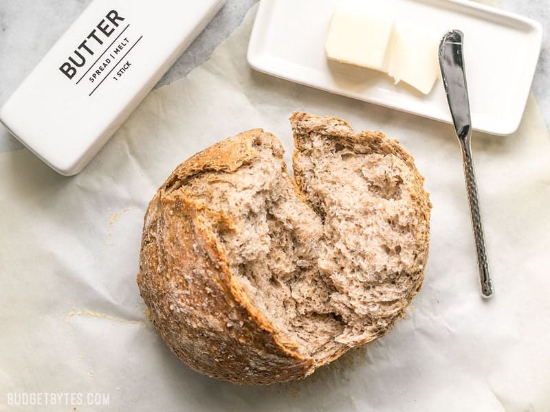 This simple homemade Seeded No-Knead Bread is packed with seeds for extra texture, flavor, and nutrients! BudgetBytes.com A loaf of Seeded No-Knead Bread next to butter