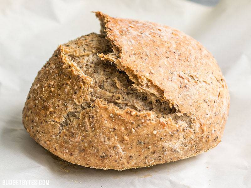 This simple homemade Seeded No-Knead Bread is packed with seeds for extra texture, flavor, and nutrients! BudgetBytes.com A whole loaf of freshly baked Seeded No-Knead Bread on parchment