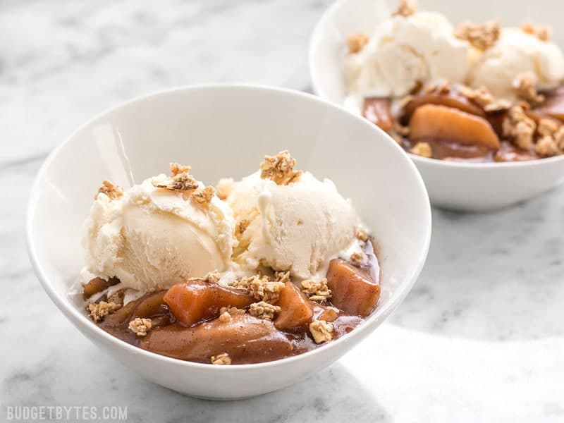 Slow Cooker Hot Buttered Apples are an easy and versatile dessert that is perfect for using up your glut of autumn apples! BudgetBytes.com Two bowls of Slow Cooker Hot Buttered Apples topped with ice cream and granola