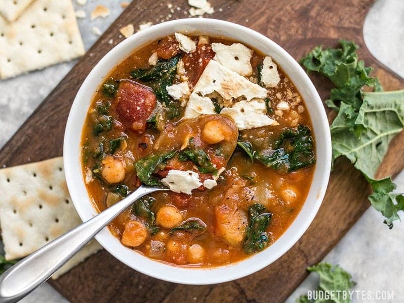 This Smoky Potato Chickpea Stew is a hearty and filling plant-based dish that will keep you full and warm this winter! BudgetBytes.com A bowl of Smoky Potato Chickpea Stew with crackers, being eaten.