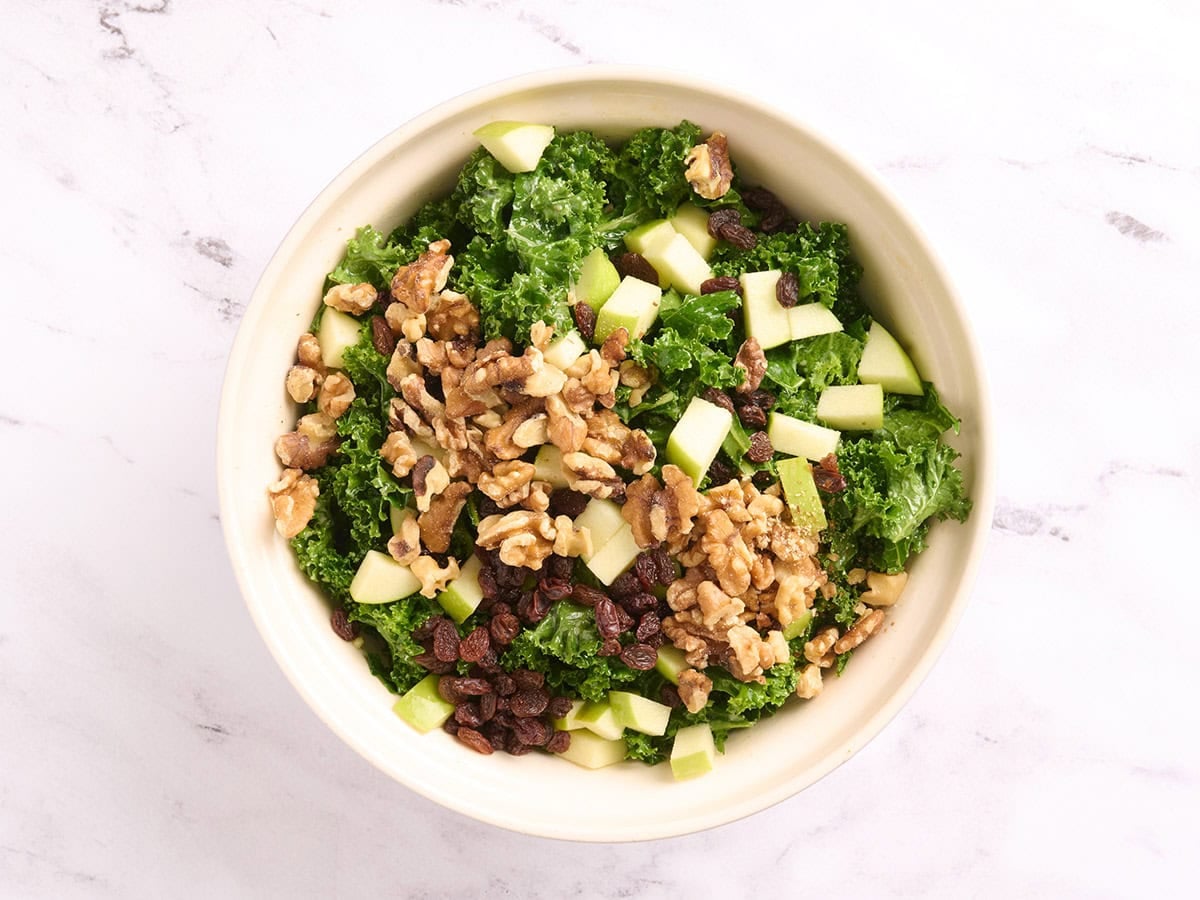 Walnuts added to a bowl with kale salad ingredients.