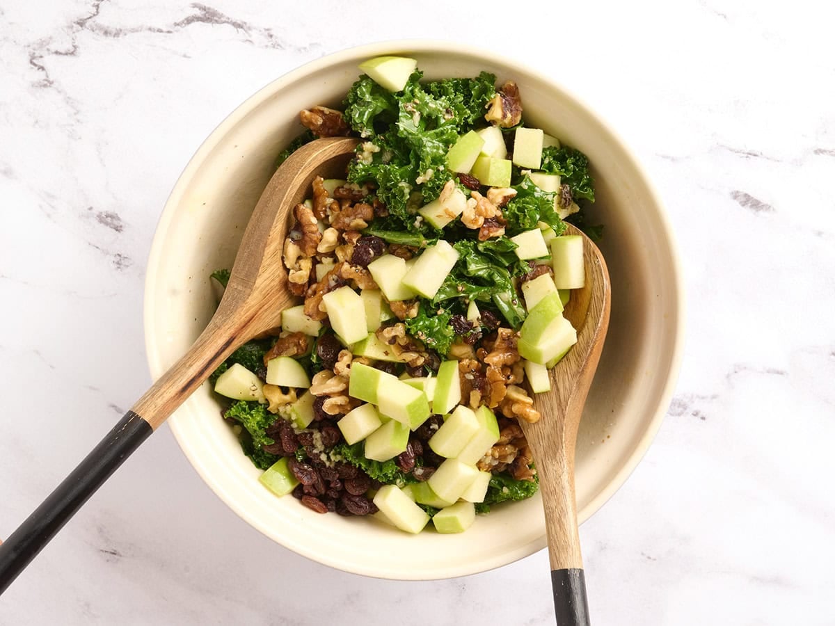 Kale salad ingredients being tossed together in a bowl.