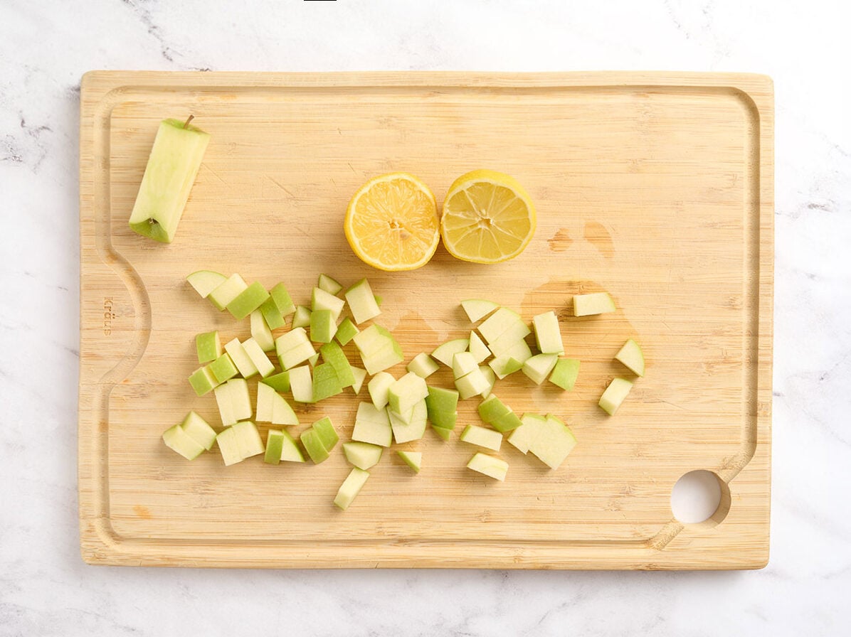 Diced apple on a cutting board with half a lemon.