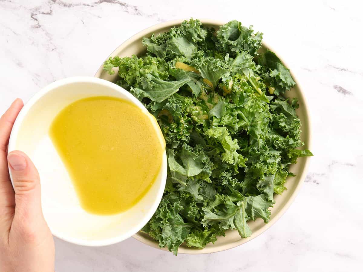 Dressing being added to kale in a bowl.