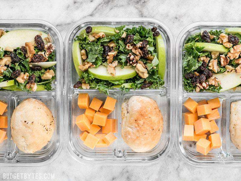 This Apple Dijon Kale Salad Meal Prep is full of texture and bright flavors, and is sure to keep you full for hours. BudgetBytes.com Three divided glass meal prep containers with Apple Dijon Kale Salad, cheddar cubes, and a dinner roll.