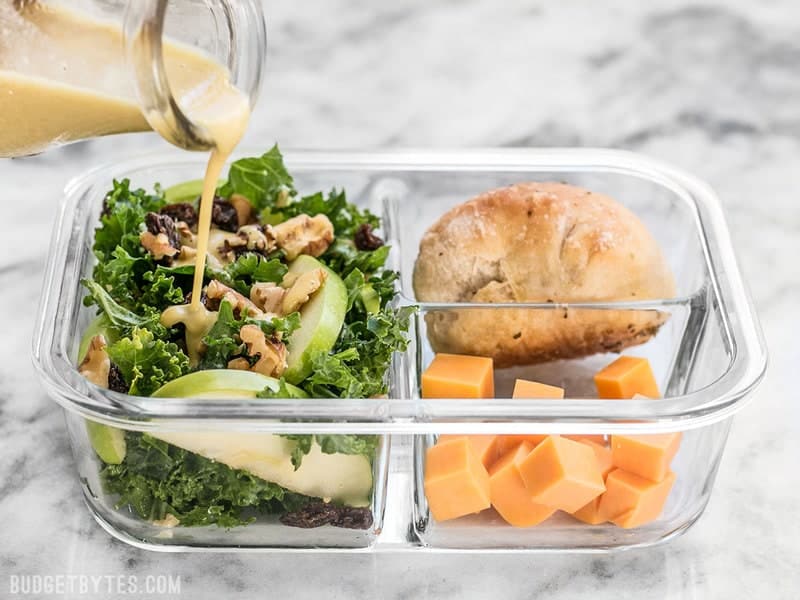 This Apple Dijon Kale Salad Meal Prep is full of texture and bright flavors, and is sure to keep you full for hours. BudgetBytes.com Dressing being poured on Apple Dijon Kale Salad