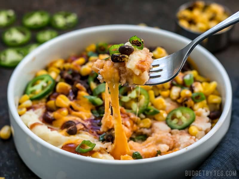 Creamy potatoes make the perfect base for a pile of colorful and flavorful toppings in these Loaded Mashed Potato Bowls. Perfect for meal prep! BudgetBytes.com A fork digging into Loaded Mashed Potato Bowls, cheese pulling