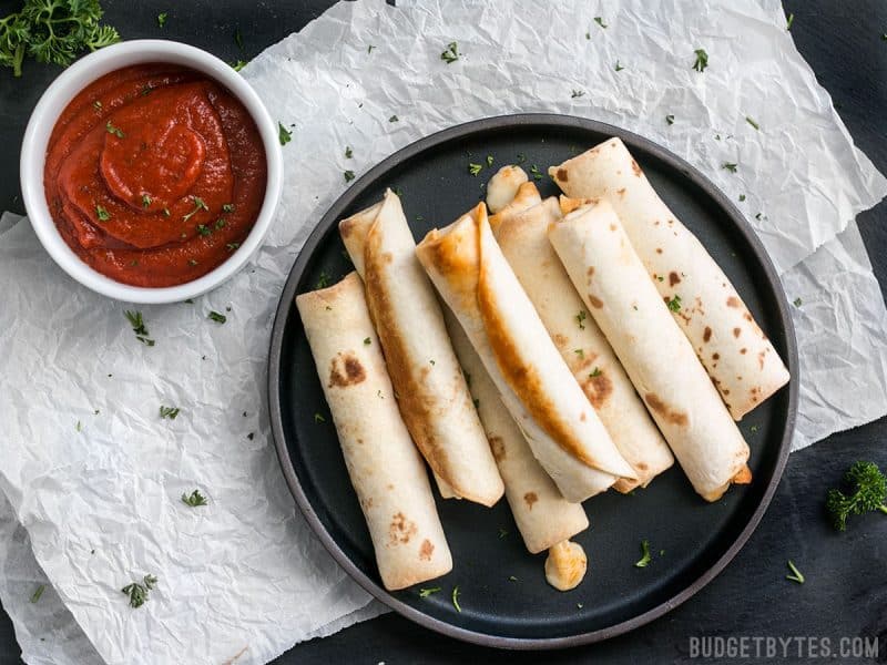 Forget frozen pizza rolls! These Pizza Roll Ups are the perfect last minute appetizer or indulgent snack on busy days! BudgetBytes.com A plate full of Pizza Roll Ups with a bowl of pizza sauce on the side