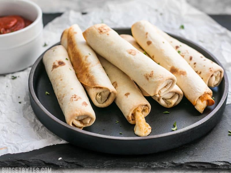 Forget frozen pizza rolls! These Pizza Roll Ups are the perfect last minute appetizer or indulgent snack on busy days! BudgetBytes.com Side view of Pizza Roll Ups on a plate with melted cheese oozing out.
