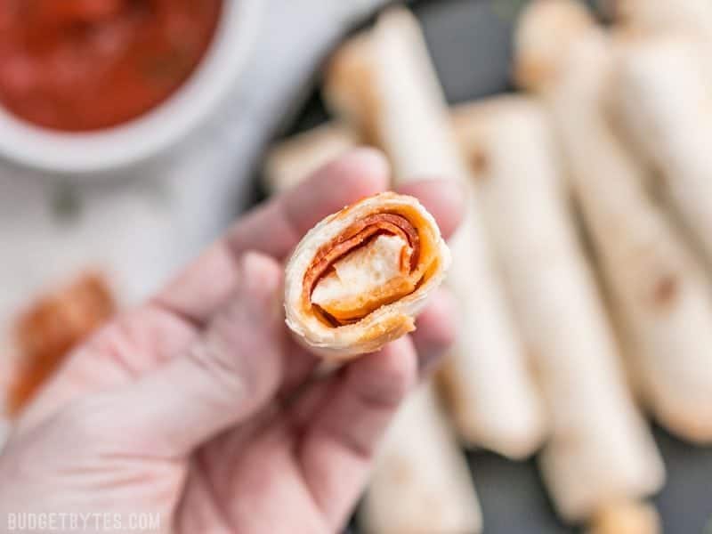 Forget frozen pizza rolls! These Pizza Roll Ups are the perfect last minute appetizer or indulgent snack on busy days! BudgetBytes.com Close up of the inside of a Pizza Roll Up being held in a hand