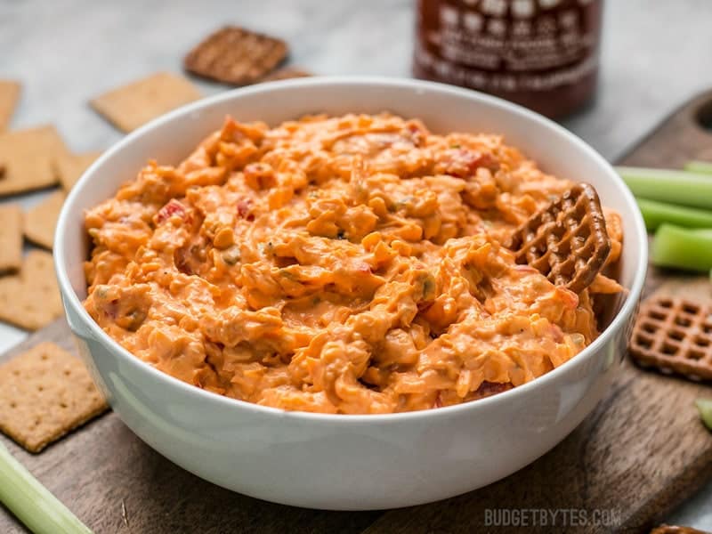 This Sriracha Pimento Cheese Spread is a rich, smoky, spicy spread with just a hint of sweetness from roasted red peppers! BudgetBytes.com A pretzel being dipped into a bowl of Sriracha Pimento Cheese Spread