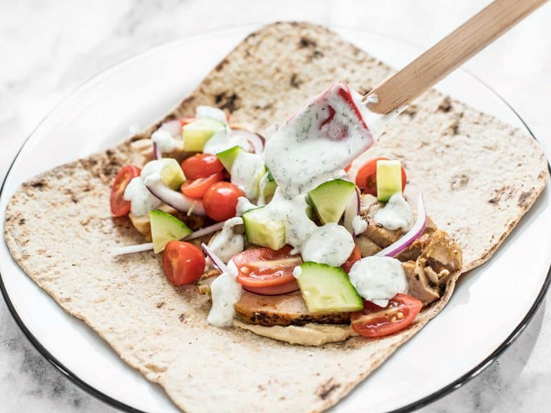 Adding the dill yogurt sauce to the flatbread with the veggies and chicken.