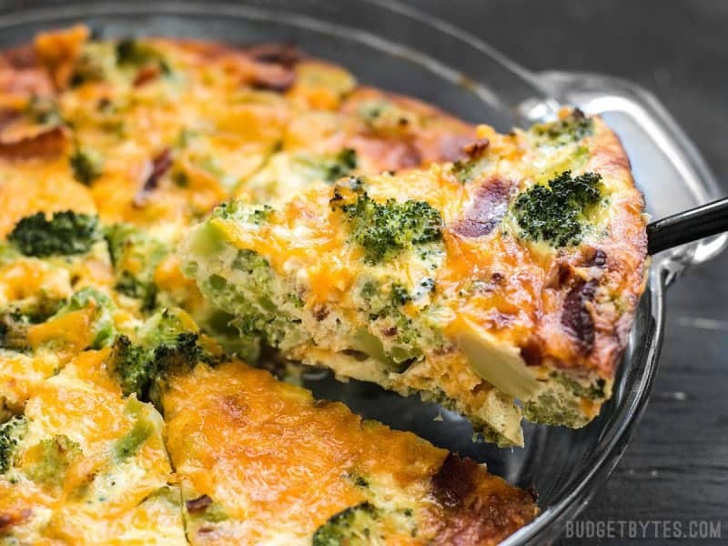 Breakfast, brunch, lunch, or dinner, this Bacon Broccoli Cheddar Crustless Quiche is an easy, filling, and customizable low-carb meal. One slice of Bacon Broccoli Cheddar Crustless Quiche being lifted out of a pie plate.