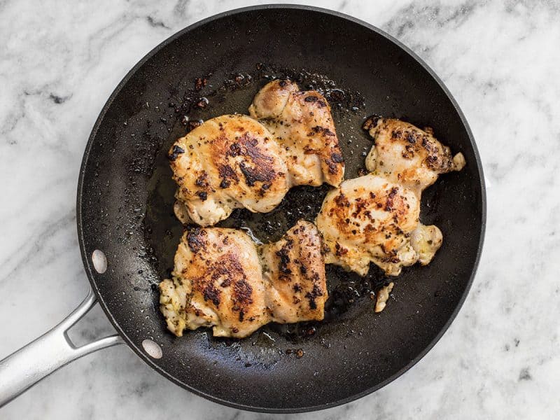 Chicken thighs cooking in a skillet.
