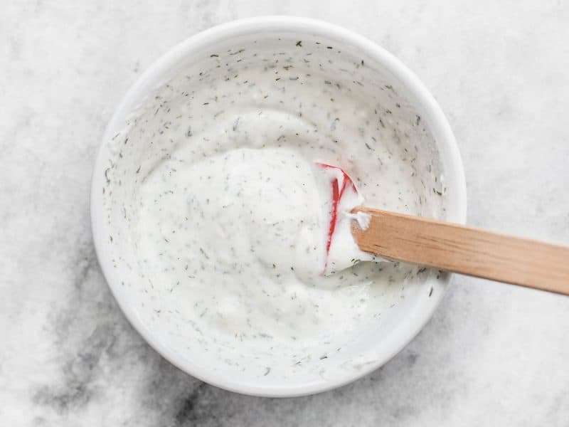 Dill yogurt sauce in a bowl with a wooden handled spoon.