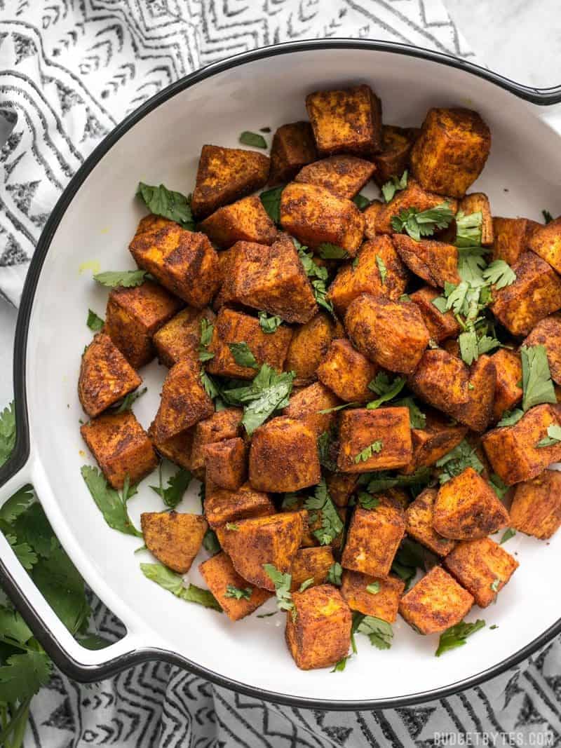 Spicy, aromatic, and earthy, these Moroccan Spiced Sweet Potatoes will add an adventurous flavor to any dinner! BudgetBytes.com A casserole dish containing Moroccan Spiced Sweet Potatoes on a patterned napkin