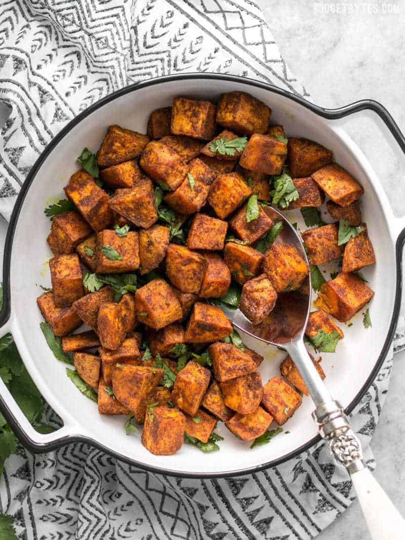 Spicy, aromatic, and earthy, these Moroccan Spiced Sweet Potatoes will add an adventurous flavor to any dinner! BudgetBytes.com Finished Moroccan Spiced Sweet Potatoes in a serving dish with cilantro