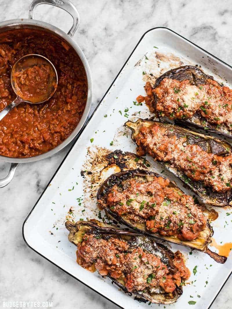 Roasted Eggplant with Meat Sauce is an elegant low carb main dish that will leave you satisfied. Pair with a simple green salad for a complete meal. BudgetBytes.com Four Roasted Eggplant with Meat Sauce on a baking sheet next to a pot full of meat sauce.