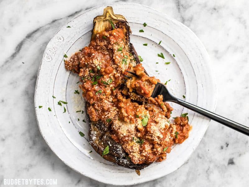 Roasted Eggplant with Meat Sauce is an elegant low carb main dish that will leave you satisfied. Pair with a simple green salad for a complete meal. BudgetBytes.com Roasted Eggplant with Meat Sauce on a white plate with a black fork scooping some up