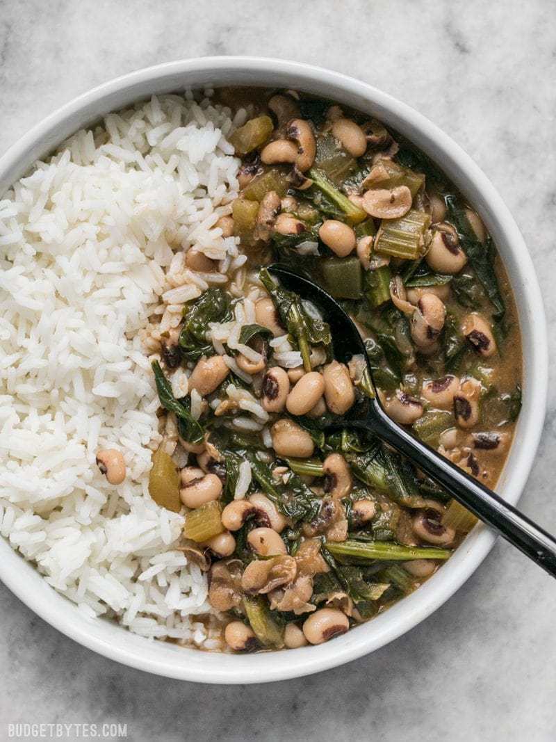 Slow Simmered Black Eyed Peas and Greens is a great cold weather comfort food that is as healthy as it is delicious! Vegan comfort food at its best! Budgetbytes.com A large bowl of Slow Simmered Black Eyed Peas with Greens, served with rice.