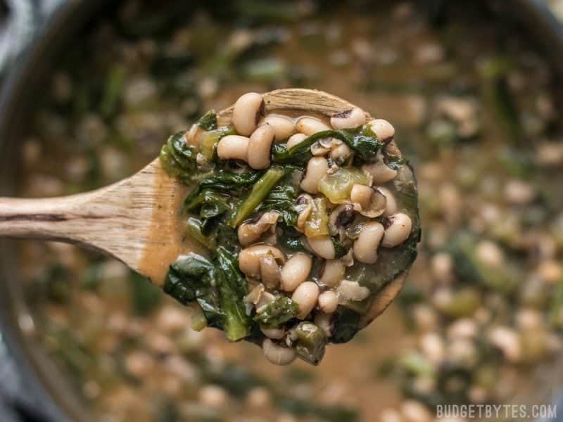 Slow Simmered Black Eyed Peas and Greens is a great cold weather comfort food that is as healthy as it is delicious! Vegan comfort food at its best! Budgetbytes.com A ladle full of Slow Simmered Black Eyed Peas with Greens