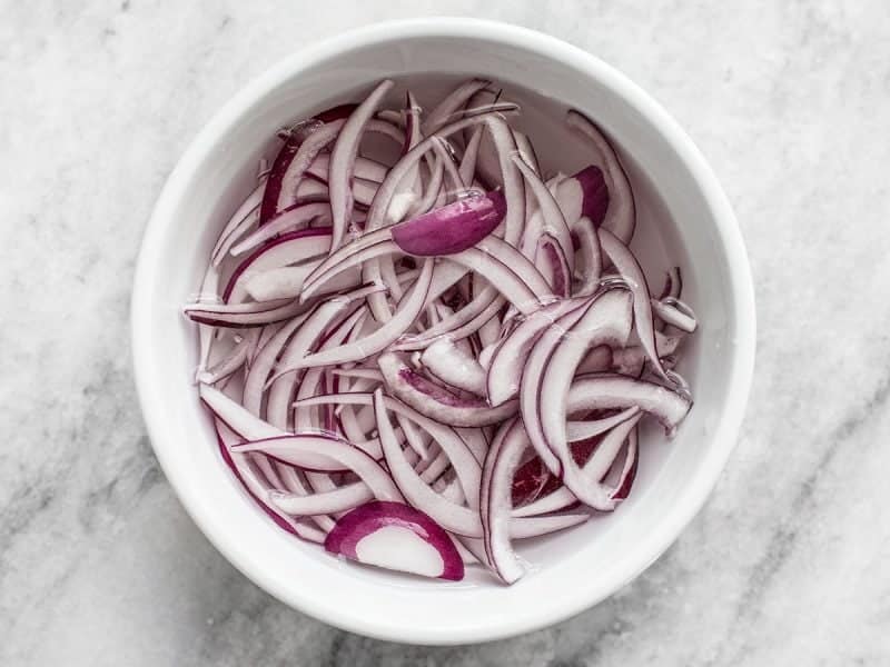 Red onions soaking in a white bowl.