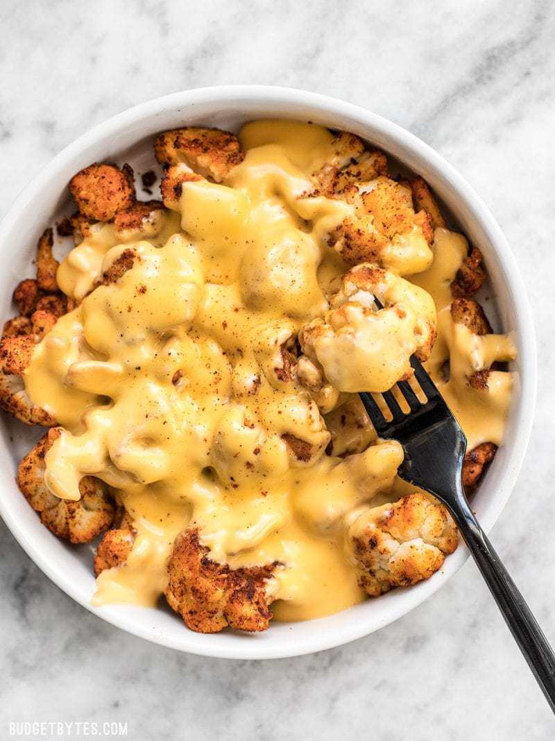 Spicy Roasted Cauliflower with Cheese Sauce is a delicious low-carb way to get your rich, creamy, cheesy fix! Step by step photos. Budgetbytes.com A big bowl of Spicy Roasted Cauliflower with Cheese Sauce being eaten with a black fork