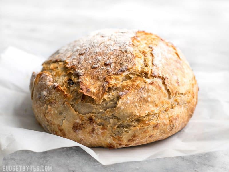 This Tomato Basil No Knead Bread is the perfect partner for your winter soups and stews, and is half the cost of a store bought artisan loaf. BudgetBytes.com Side view of freshly baked Tomato Basil No Knead Bread