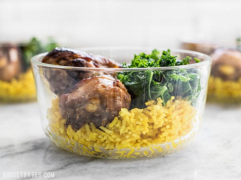 This Chicken Adobo Meal Prep combines overnight marinated chicken, rice cooked with warm spices, and simple sautéed kale for a well rounded and filling meal. BudgetBytes.com Side view of a Chicken Adobo Meal Prep container