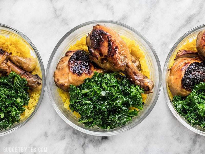 This Chicken Adobo Meal Prep combines overnight marinated chicken, rice cooked with warm spices, and simple sautéed kale for a well rounded and filling meal. BudgetBytes.com Three glass Chicken Adobo Meal Prep containers in a row