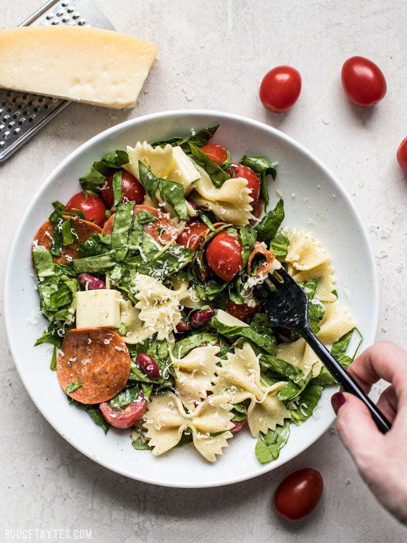 Pepperoni’s rich and peppery bite is the perfect contrast to mild spinach, mozzarella, and pasta in this Pepperoni Pasta Salad. BudgetBytes.com Pepperoni Pasta Salad being eaten with a black fork. Parmesan and tomatoes near by.