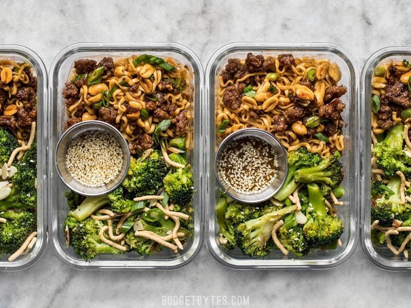 A little bit indulgent, a little bit healthy, this Pork and Peanut Dragon Noodle Meal Prep is a flavorful, filling, and DELICIOUS lunch! BudgetBytes.com Four rectangular glass meal prep containers with Pork and Peanut Dragon Noodles, broccoli salad, and containers of salad dressing.