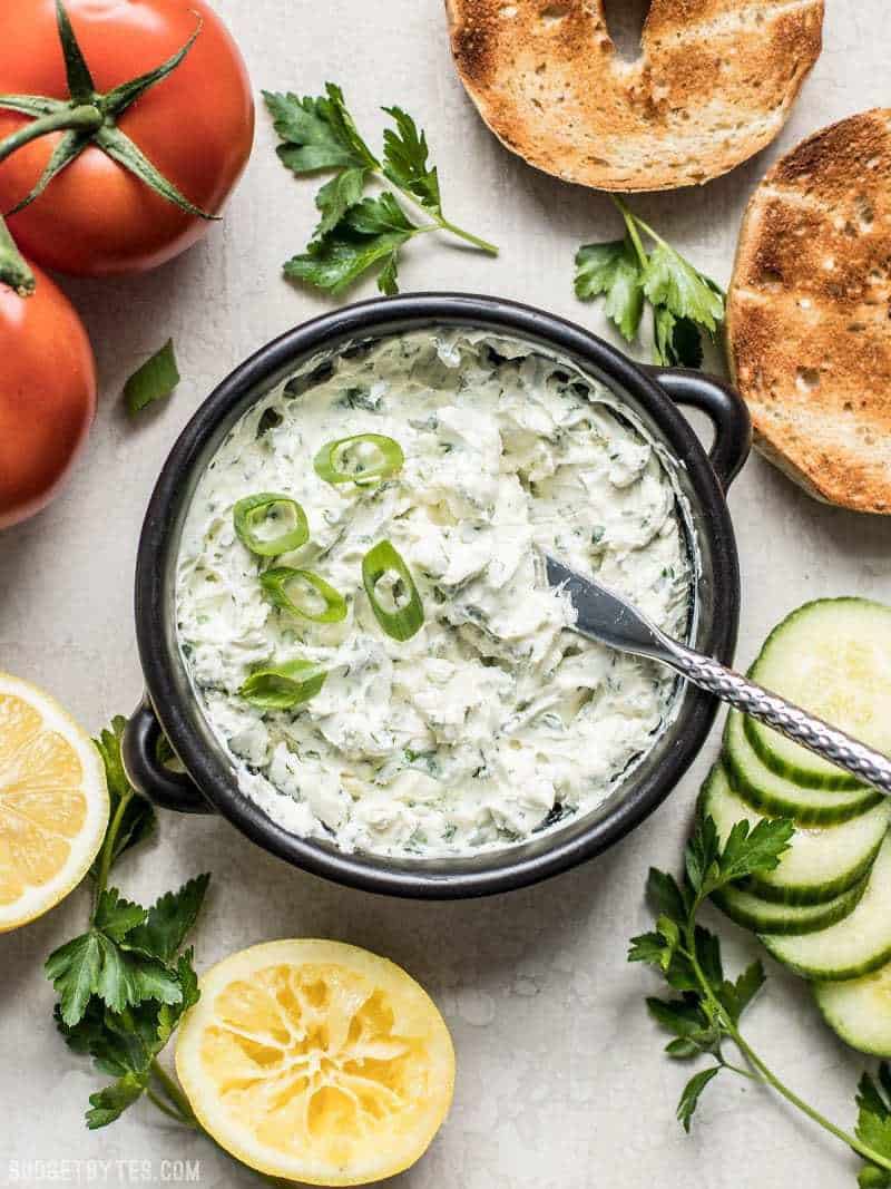 This tangy, herb-infused Scallion Herb Cream Cheese Spread is perfect for sandwiches, wraps, or even snacking on fresh vegetables. BudgetBytes.com A bowl of Scallion Herb Cream Cheese Spread surrounded by vegetables, bagels, and lemons