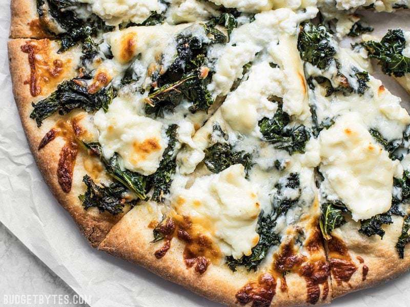 Garlicky greens and creamy ricotta pair perfectly on this light and fresh Garlicky Kale and Ricotta Pizza. It’s the perfect pizza for summer! BudgetBytes.com Close up view of browned crust and cheese on Garlicky Kale and Ricotta Pizza