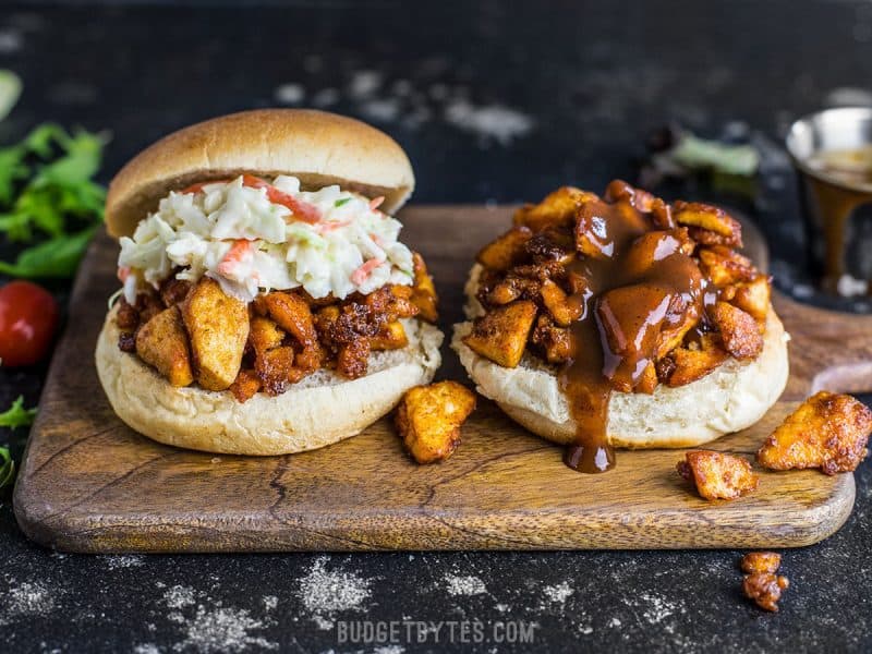 BBQ Tofu Sliders are an easy and inexpensive alternative to pulled meat sandwiches. With a simple ingredient list, this is a tofu dish anyone can master! Front view of two BBQ Tofu Sliders on a wooden cutting board, sauce dripping down the front