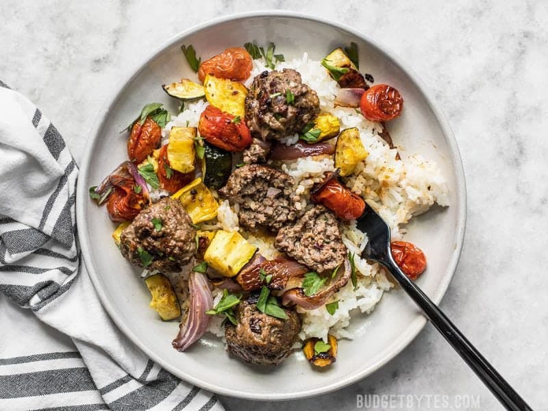 Beef Kofta Meatballs with Roasted Vegetables are the perfect well-rounded easy dinner or meal prep to keep you fed and happy throughout the week. BudgetBytes.com Beef Kofta Meatballs with Roasted Vegetables on a stoneware plate with a black fork and striped napkin