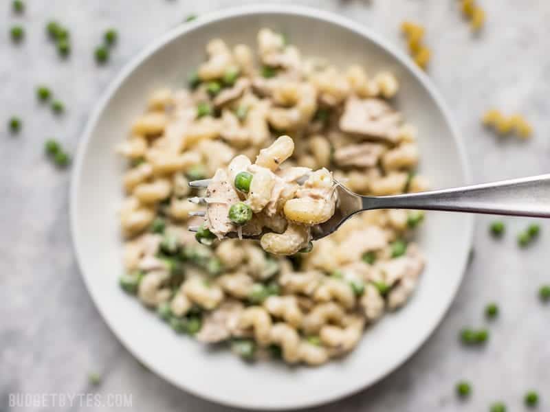 This quick and comforting Creamy Tuna Pasta with Peas and Parmesan is a fast and easy weeknight dinner that only requires a few simple ingredients. Budgetbytes.com Close up view of a forkful of Creamy Tuna Pasta with Peas and Parmesan with the bowl in the background