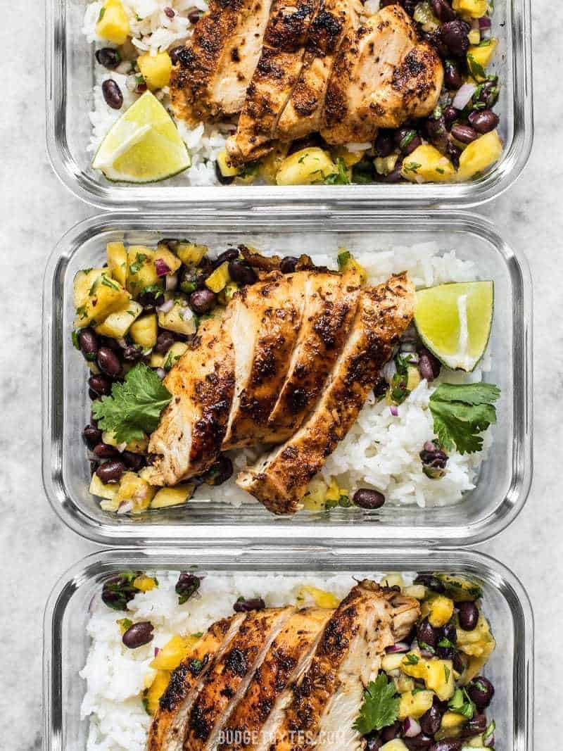 Full of fresh summery flavor, with just a few ingredients, this Jerk Chicken with Pineapple Black Bean Salsa will become your new go-to easy summer meal! Rectangle glass meal prep containers full of Jerk Chicken with Pineapple Black Bean Salsa, rice, and limes.
