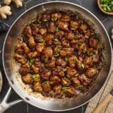 Overhead view of easy sesame chicken, topped with sliced green onions in a skillet.