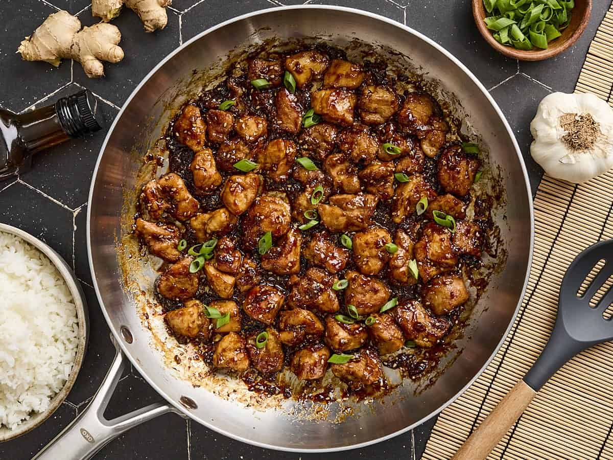 Overhead view of easy sesame chicken, topped with sliced green onions in a skillet.