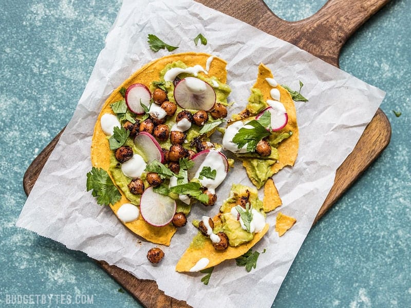 These cool and refreshing Spiced Chickpea Tostadas are the perfect almost no cook dinner for summer. Customize the toppings based on what you have on hand to make the most of leftovers! Budgetbytes.com A Spiced Chickpea Tostada on a piece of parchment, broken into pieces