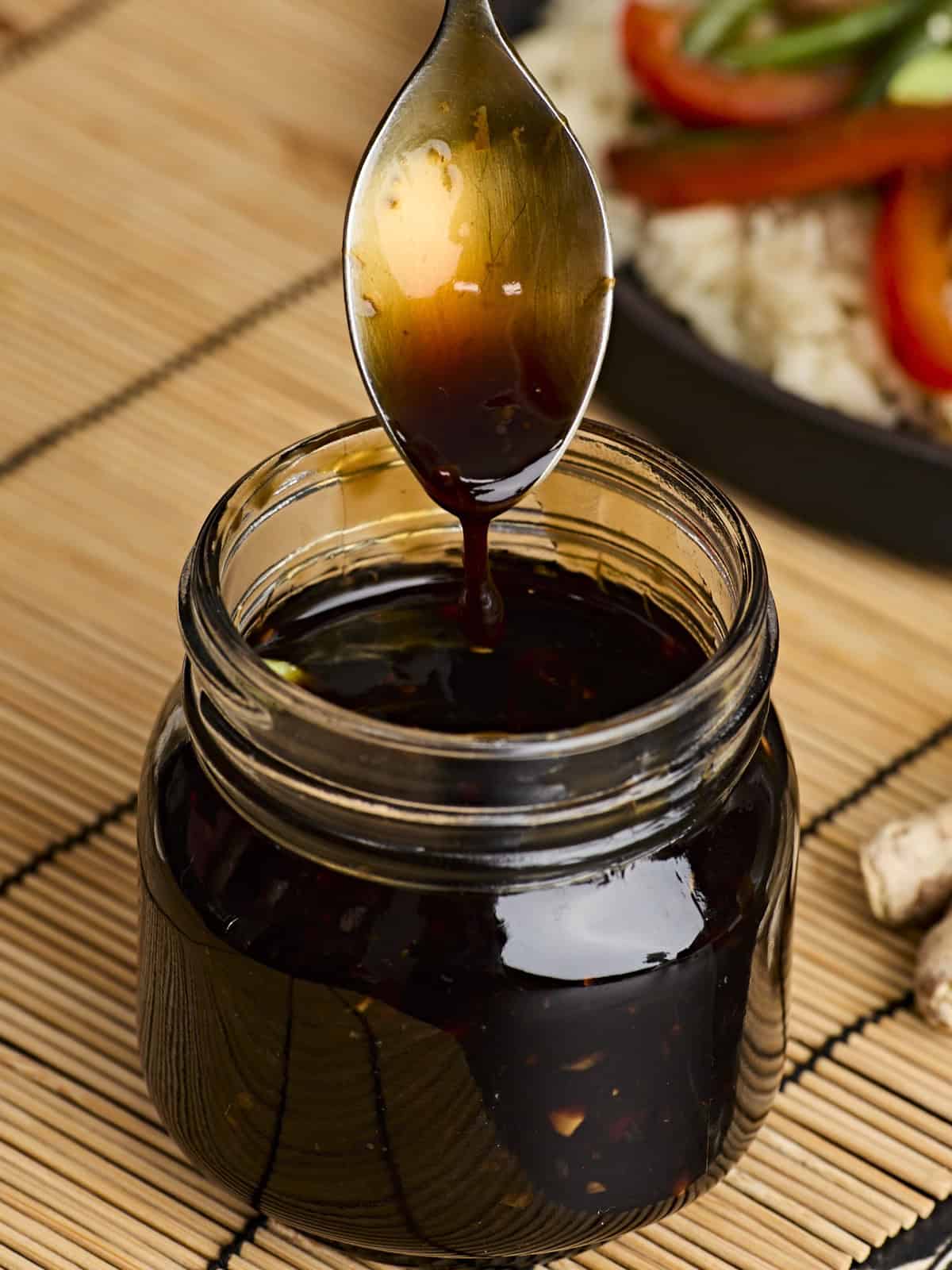 This Easy Homemade Teriyaki Sauce (or marinade) takes only a few minutes and five simple ingredients that can be kept on hand at all times. Perfect for last minute weeknight dinners! Budgetbytes.com Side view of a glass jar of easy homemade teriyaki sauce, with a spoon dipped in.