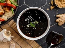 Overhead view of a bowl of homemade teriyaki sauce, topped with sesame seeds and sliced green onion.