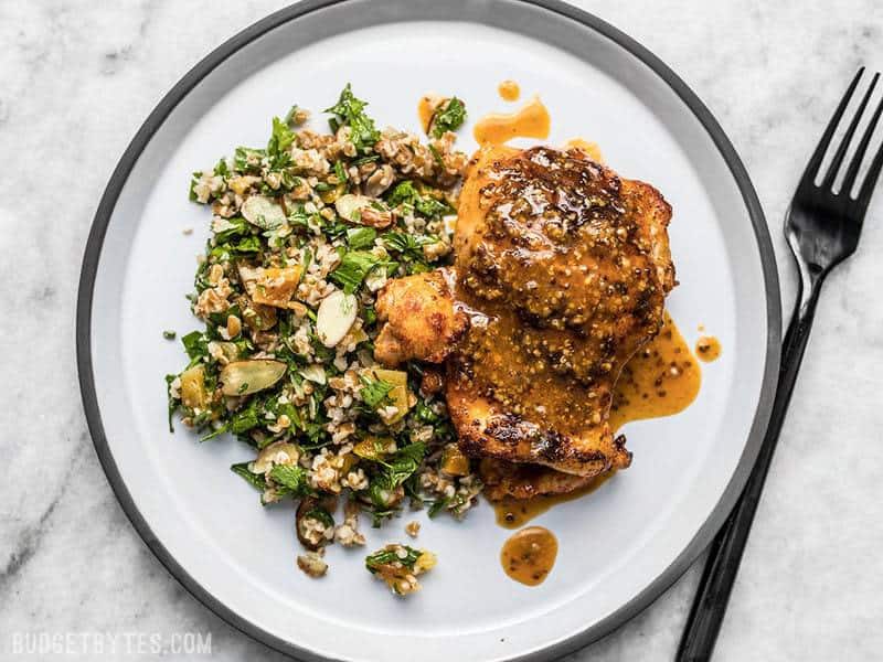 This sweet and tangy 20 Minute Honey Mustard Chicken will be your new family favorite weeknight dinner. Only a few pantry staples needed! Budgetbytes.com A plate of honey mustard chicken with pan sauce drizzled over top and parsley almond salad on the side.