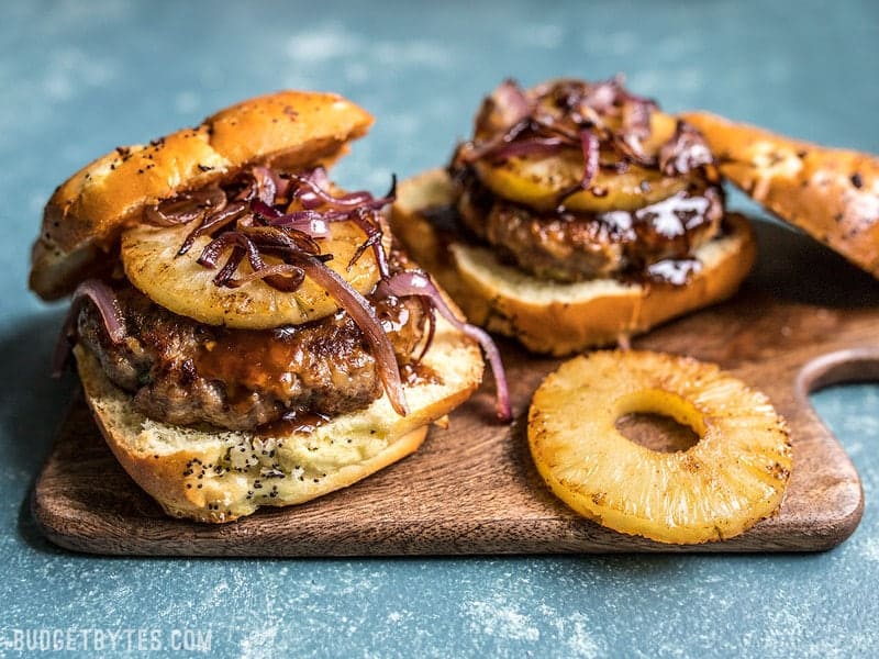 These rich and juicy Hawaiian Burgers are flavored with sweet pineapple, tangy teriyaki sauce, savory green onions, and creamy Monterey jack cheese. Budgetbytes.com Front view of Hawaiian Burgers topped with Pineapple rings and caramelized onions
