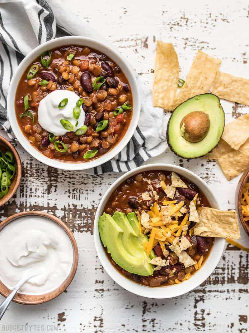 This Slow Cooker Vegetarian Lentil Chili makes a huge batch, is packed with flavor and nutrients, and can be made for only about 5 dollars! Budgetbytes.com Two bowls of slow cooker vegetarian chili with chips and other toppings